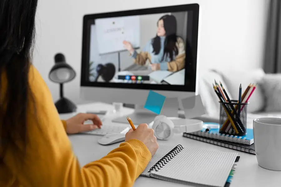 Person taking notes during an online class on a desktop computer.